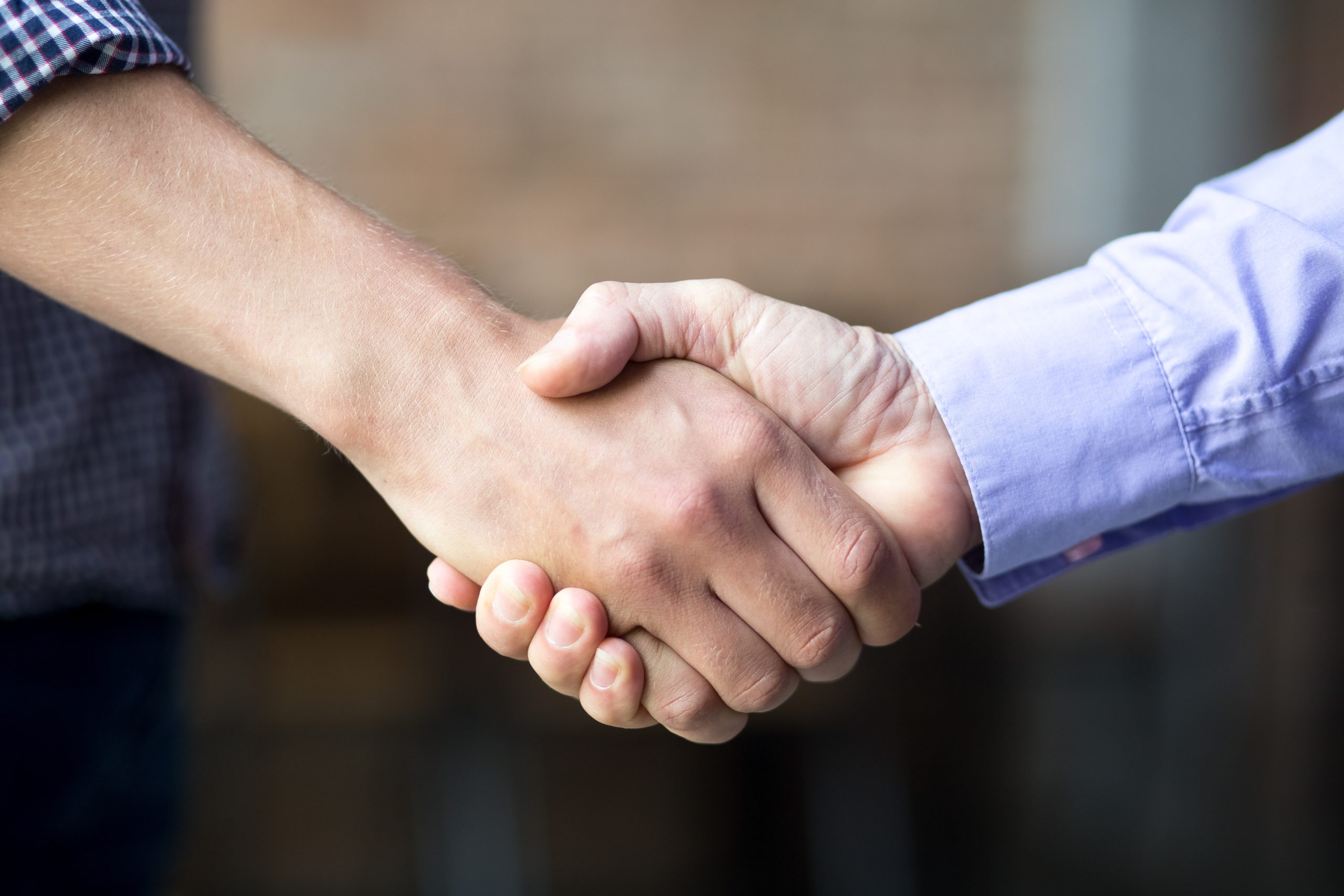 Cropped view of two business men shaking hands with blurred view in background. Side view.